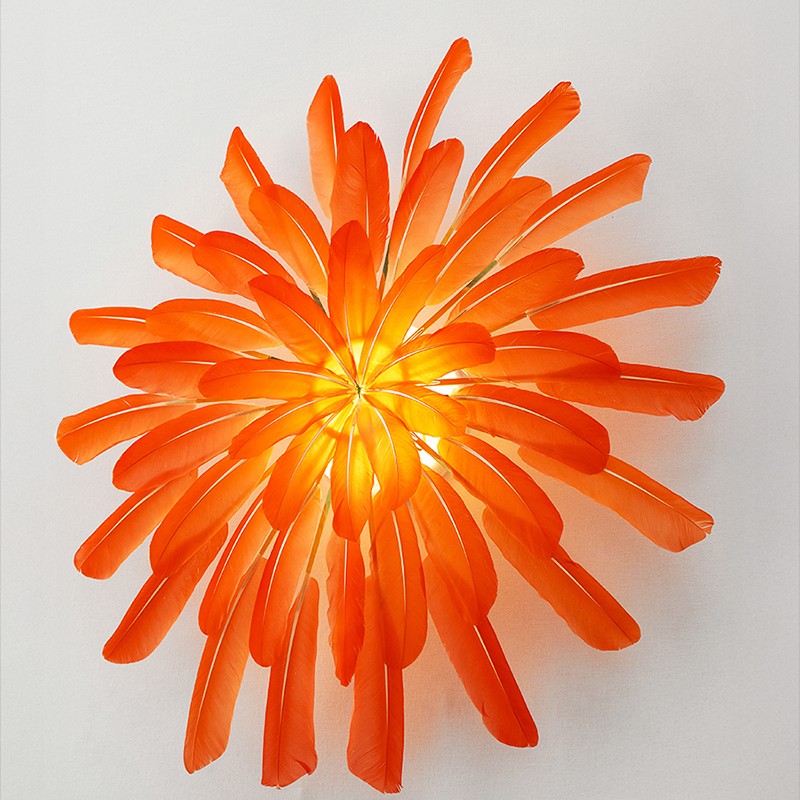 Illuminated vermillion feathers are composed into a wall sconce by French artist Janaïna Milheiro & radiate with a warm glow, available through RUNE, New York.